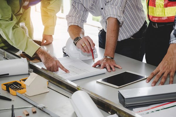 construction worker team planning about building plan with blueprint, safety helmet, construction tools on conference table at construction site, contractor, business, industry, construction concept